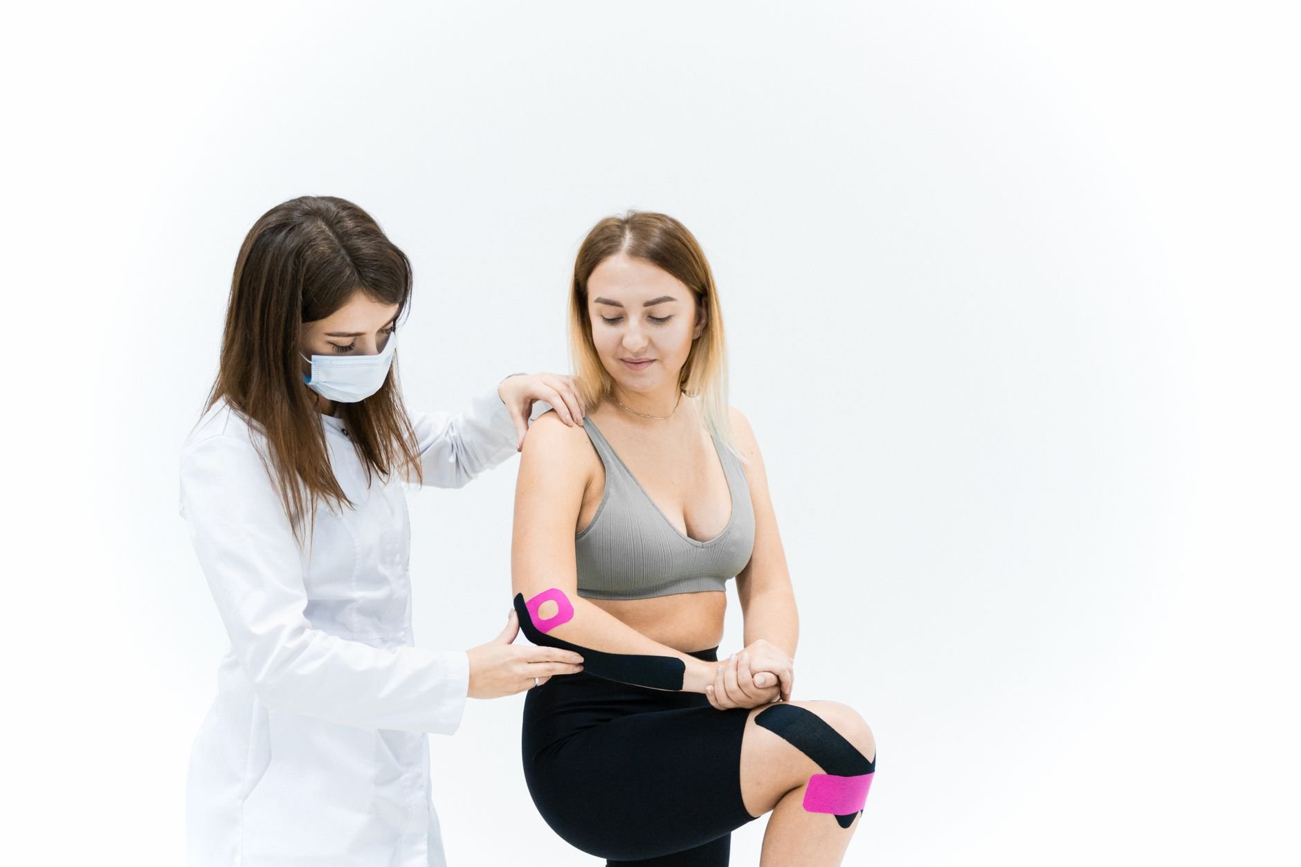 A therapist applies kinesio tape on a woman's knee during a physical therapy session.